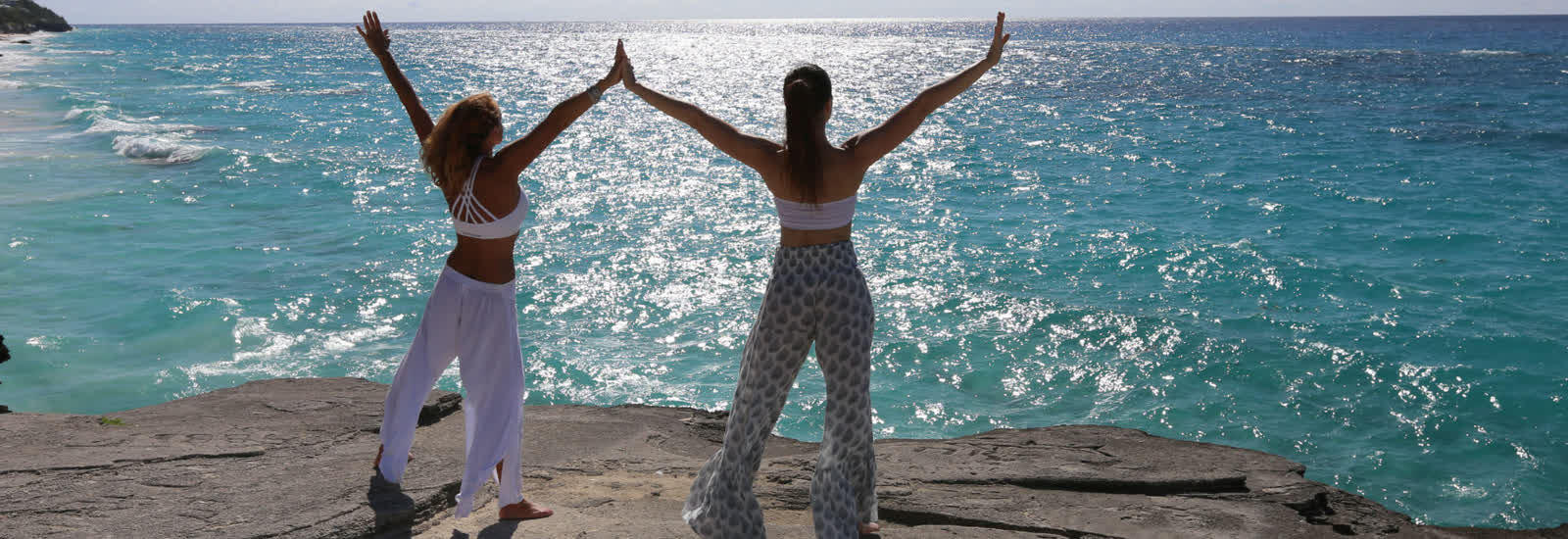 Two women standing on a rock with arms raised above a sunlit ocean